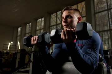 Contemporary young athlete holding heavy dumbbells in both hands while exercising in cross training center