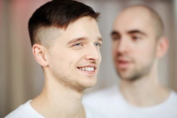Happy young man with short cut hair and his bald gay partner on background