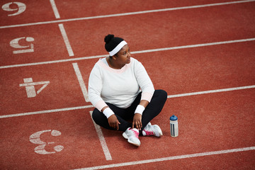 Obraz premium Pensive female in activewear sitting on one of stadium race tracks after training