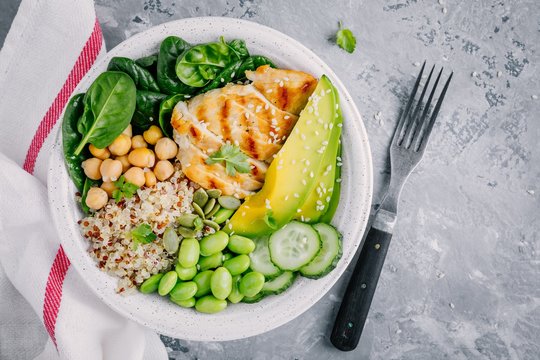 Buddha bowl salad with spinach, quinoa, roasted chickpeas, grilled chicken, avocado, edamame beans, cucumbers, sesame and pumpkin seeds.