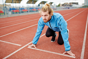 Obraz premium Young determined man in sportswear standing by start line on race track