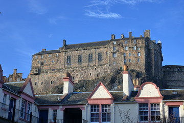 Widok zamku w Edynburgu, Szkocja, na szczycie skalistego wzgórza, na pierwszym planie dachy budynków w Edynburgu, słonecznie, piękne, bezchmurne błękitne niebo - obrazy, fototapety, plakaty