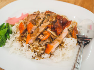 Thai rice with roasted duck in white plastic dish served on wooden table.