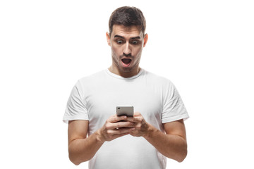 Handsome young man in white t-shirt, holding smartphone, looking scared and confused reading text message or e-mail