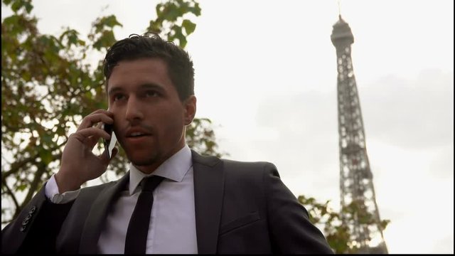 Attractive young man in a suit takes a selfie on a smartphone next to the Eiffel Tower