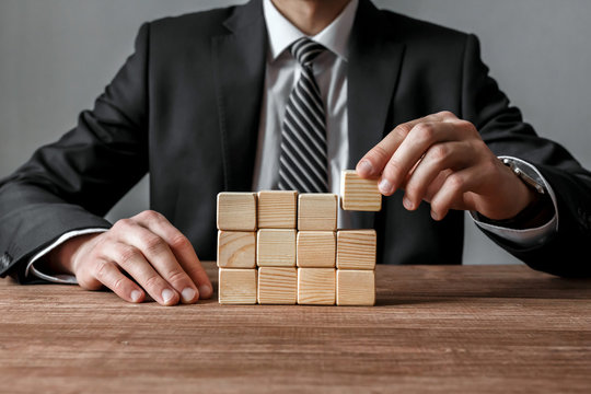 Businessman building a structure with wooden cubes on table.Success and business strategy concept.