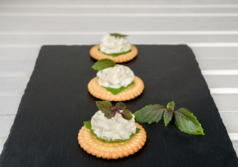 Biscuit cracker appetizer with cream cheese and basil topping