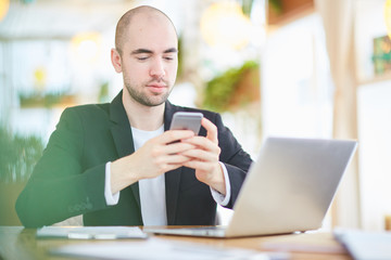 Businessman with mobile phone and laptop sitting at cafe