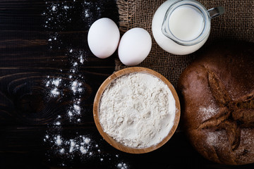 Freshly baked homemade bread with milk, flour  and eggs on a black background, top view.