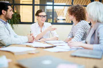 One of young economists explaining her point of view to colleagues at start-up meeting in office