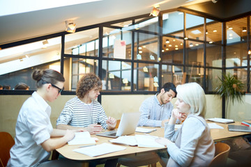 Several young managers working individually while sitting by table in boardroom