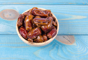 Dry dates fruit in the bowl, on the wood background.