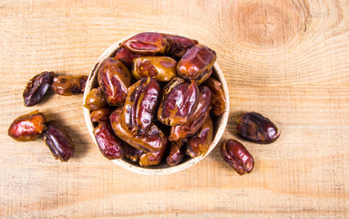 Dry dates fruit in the bowl, on the wood background.