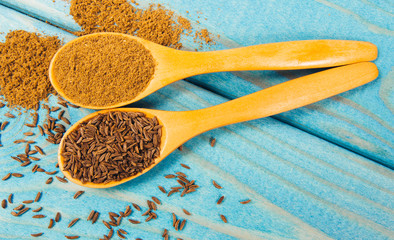 Ground cumin in a spoon and whole cumin on the wooden background.