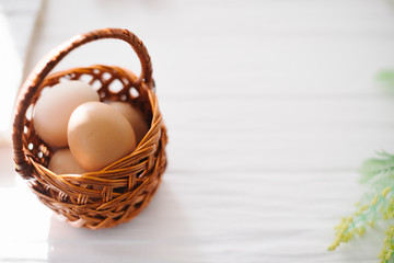 Eggs in a wicker basket on a white wooden background