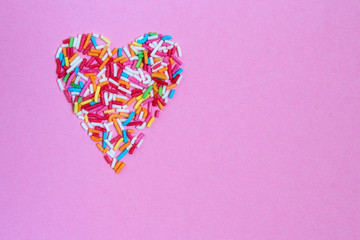 Heart from multi-colored confetti on a pink background flat  lay layout from above