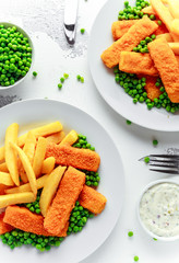 British Traditional Fish finger and chips with peas and tartar sauce in a white plate.