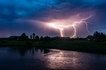 Thunderstorm and lightning over the night village on the river bank