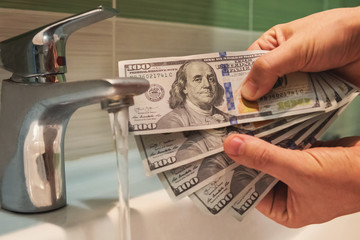US dollars hung under running tap water