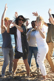 Young excited friends dancing on sandy beach on summer weekend