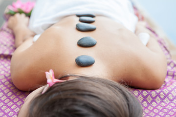 Closeup on young woman having hot stone massage on back in spa