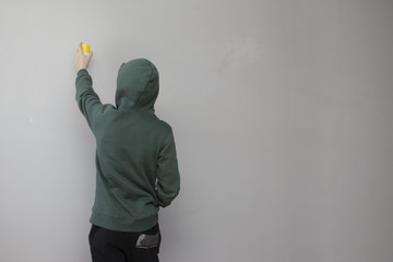 A teenager holding a yellow spray paint in front of a gray wall