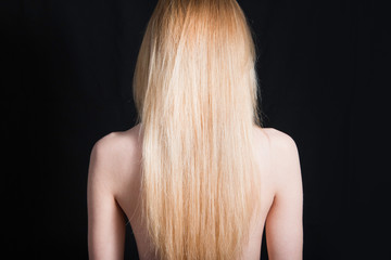 Fototapeta premium Back view of young girl with beautiful long blonde hair isolated on black