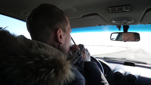 The driver of an alcoholic drinks cognac while driving a car. A man of 50 years is driving a car and drinking alcohol from a flask.