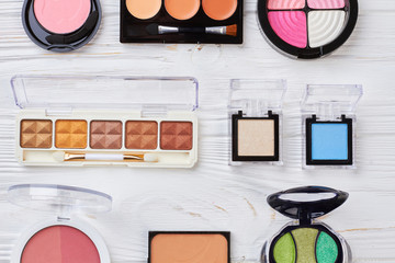 Multicolored eyeshadows collection, top view. Set of female decorative cosmetics palette on white wooden background. Femininity and beauty concept.