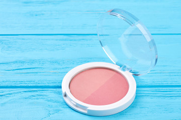 Blusher in compact box, wooden background. Face blush powder on blue wooden background. Beauty make up product.