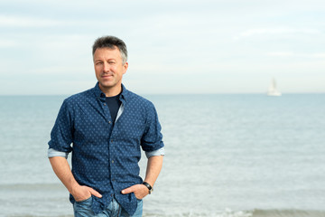 Handsome middle-aged man walking at the beach. Attractive mid adult male model posing at seaside in blue jeans, t-shirt shirt. Outdoor portrait of beautiful macho man.
