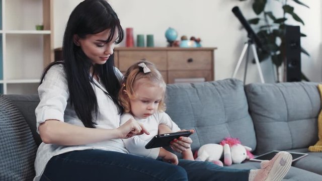 mom and daughter sit on sofa use phone look some interesting hug woman baby hand love child girl kid internet cartoon technology smartphone face home mobile touch mother game little play application