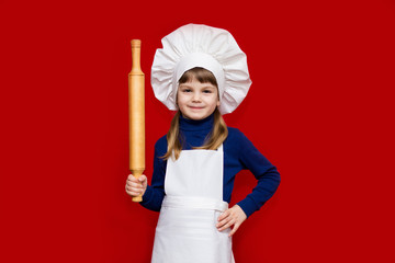 Happy little girl in chef uniform holds rolling pin isolated on red. Kid chef. Cooking Process Concept 