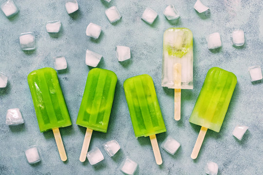 Refreshing Frozen Fruit Green Juice On A Stick With Slices Of Ice On A Blue Background. Healthy Eating. View From Above. Cooling Frozen Juice In Hot Weather.