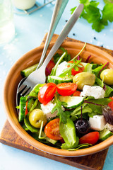 Summer vitamin salad. Greek salad close-up with fresh vegetables, feta cheese and black olives on a blue stone or concrete table.