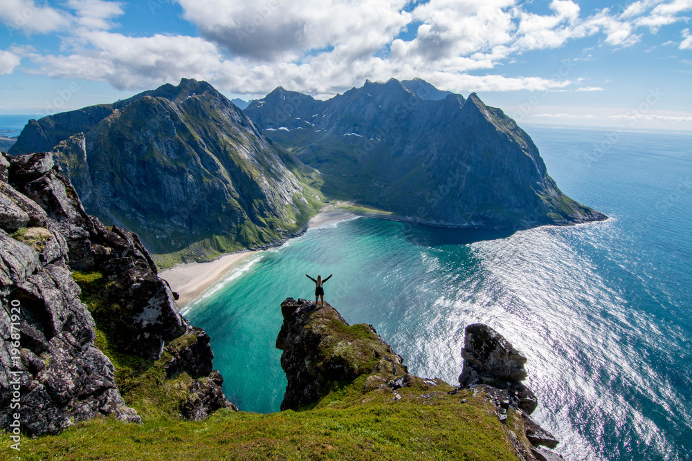 Wall mural adventurous woman looking down at kvalvika beach in lofoten, norway