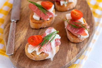 Italian prosciutto and feta cheese bruschetta decorated by tomato and dill. Antipasti on grilled baguette bread.
