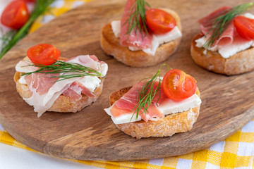 Italian prosciutto and feta cheese bruschetta decorated by tomato and dill. Antipasti on grilled baguette bread.