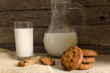 Oatmeal chocolate chip cookies, jug and glass of milk, rustic wooden background.