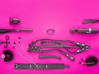 Various toys for adults (leather harness, collar with clips, anal plug, fur handcuffs, vibrator and other) are on a purple background. The image is suitable for the banner of the sex store goods