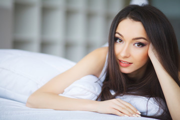Obraz na płótnie Canvas Happy morning. Portrait of a smiling pretty young brunette woman relaxing in white bed.