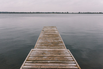 Jetty on the river. A long wooden pier for boats and yachts against a cloudy sky.