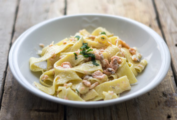Homemade italian pasta with smoked salmone and creamy sauce and parsley on the top, white plate on the wooden rustic table