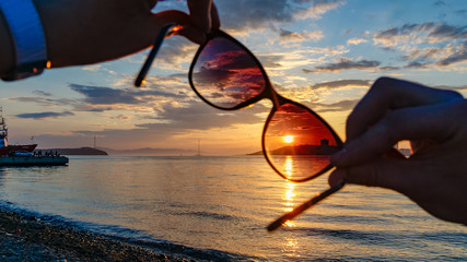 Fototapeta na wymiar Sunset through the sun glasses in hands, sea background