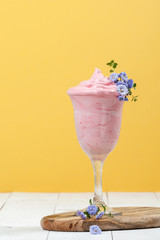 Strawberry smoothies in a high glass on a wooden table on a yellow background..