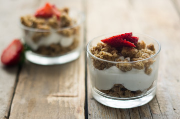 Little glass bowl of homemade granola with greek yoghurt and strawberries, isolated on the wooden rustic table