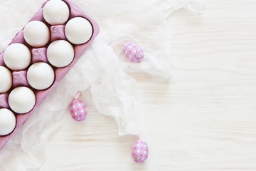 Fototapeta na wymiar Top view of white eggs and pink colored Easter eggs r on white wooden background. Top view, Easter concept, greeting card