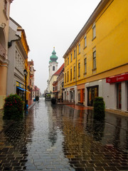 Fototapeta na wymiar Hungary, Gyor - August 31, 2014: Kazinczy utca (street) in Gyor on a rainy summer-autumn day. A deserted Hungarian street with ancient low houses and wet paving stones from the rain