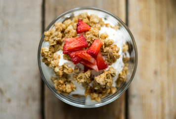 Little glass bowl of homemade granola with greek yoghurt and strawberries, isolated on the wooden rustic table. Flat lay.