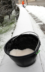 bucket of salt used to melt ice and snow from the sidewalk and the street sweeper in the background